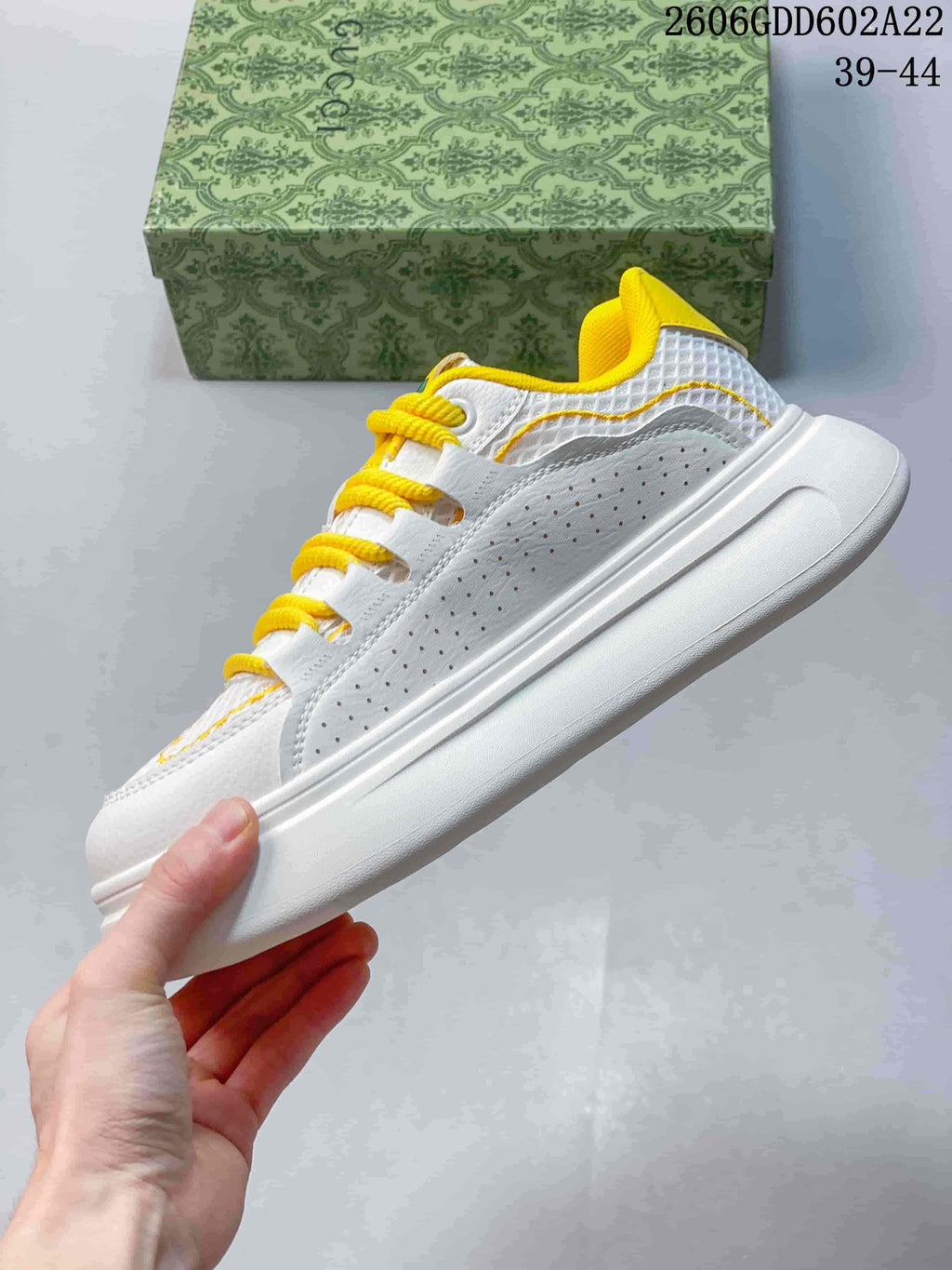 Side view of the white sneaker with yellow stitching and a thick sole