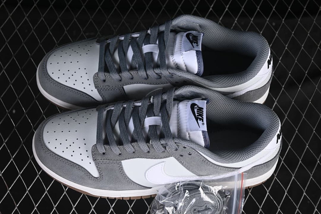 Pair of white and grey Nike SB Dunk Low shoes viewed from above, showing perforated toes and grey laces