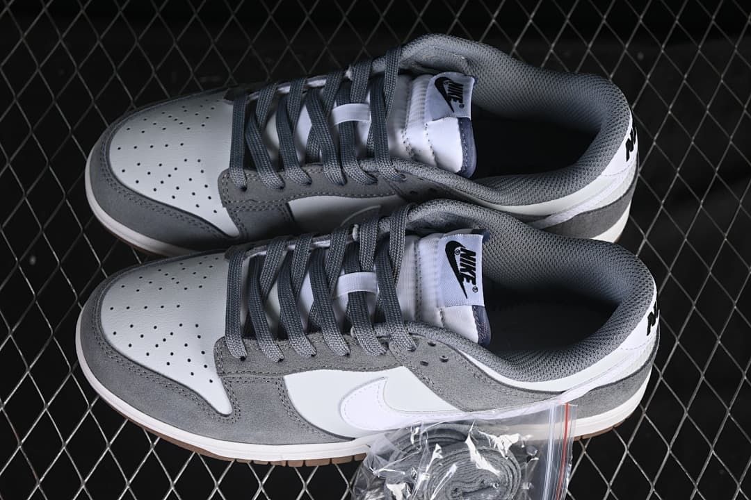 Pair of white and grey Nike SB Dunk Low shoes viewed from above, showing perforated toes and grey laces