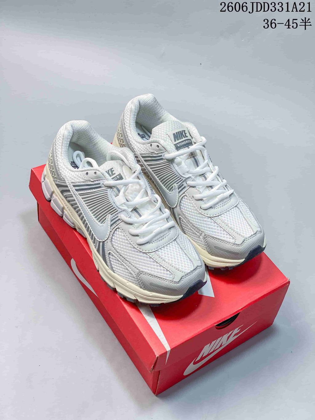 Pair of white and grey Nike Zoom Vomero 5 sneakers displayed on a red shoe box