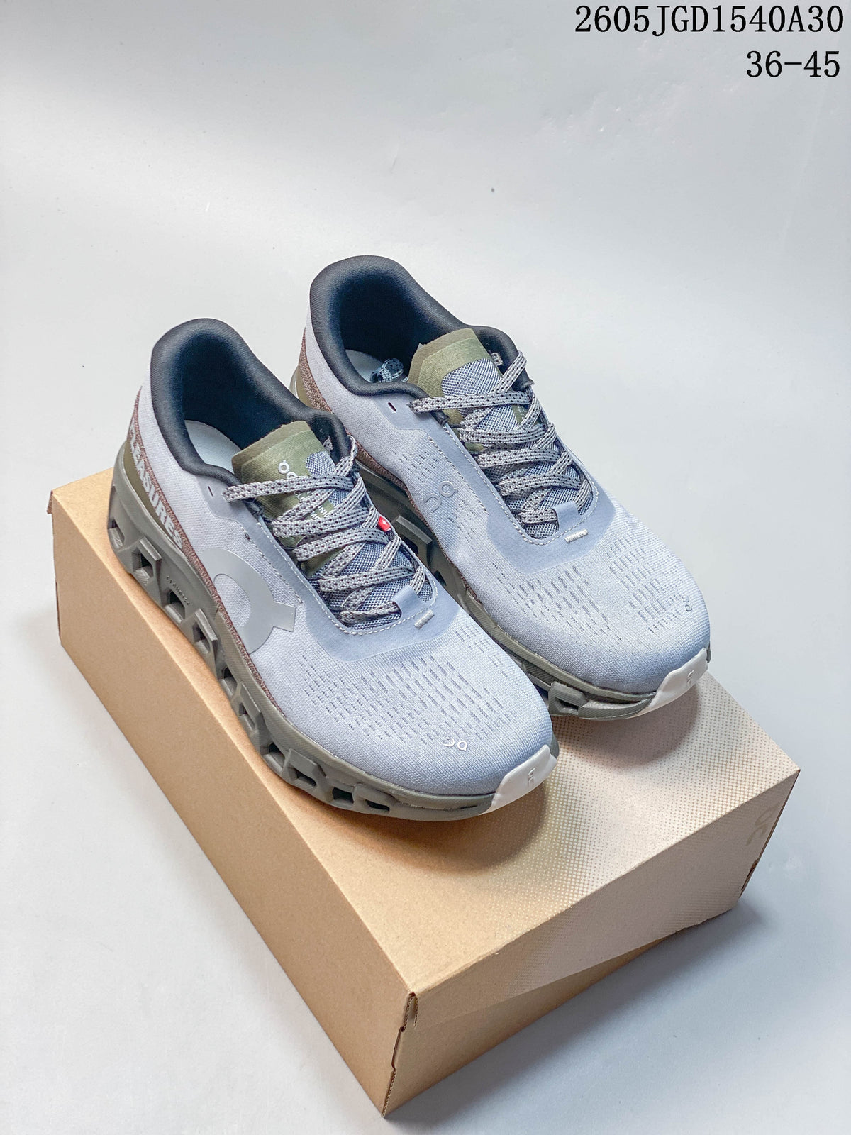 Pair of pale gray On Cloudmonster Void low-top sneakers with olive and muted rose accents, shown on a box
