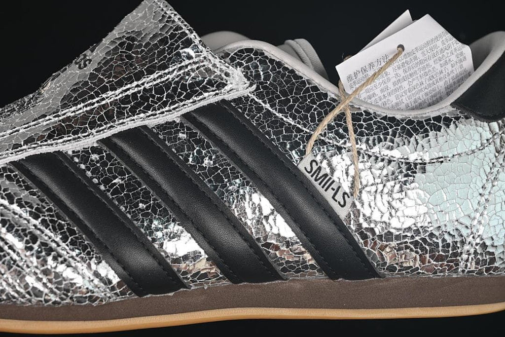 Close-up of silver crackle-pattern upper, black stripes and the wide forefoot strap.