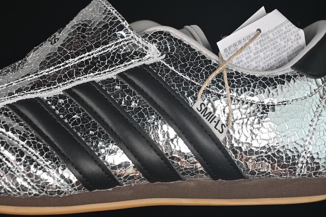 Close-up of silver crackle-pattern upper, black stripes and the wide forefoot strap.