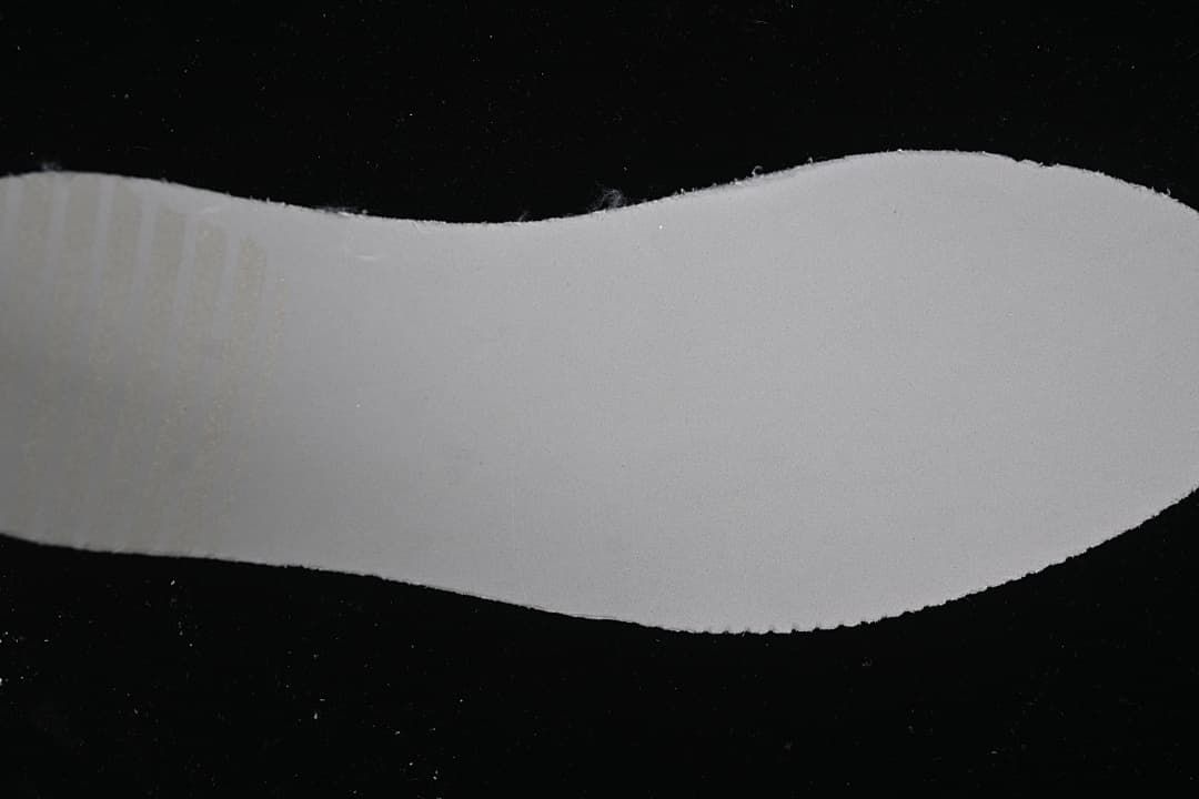 Close-up view of a plain white shoe component against a dark background.