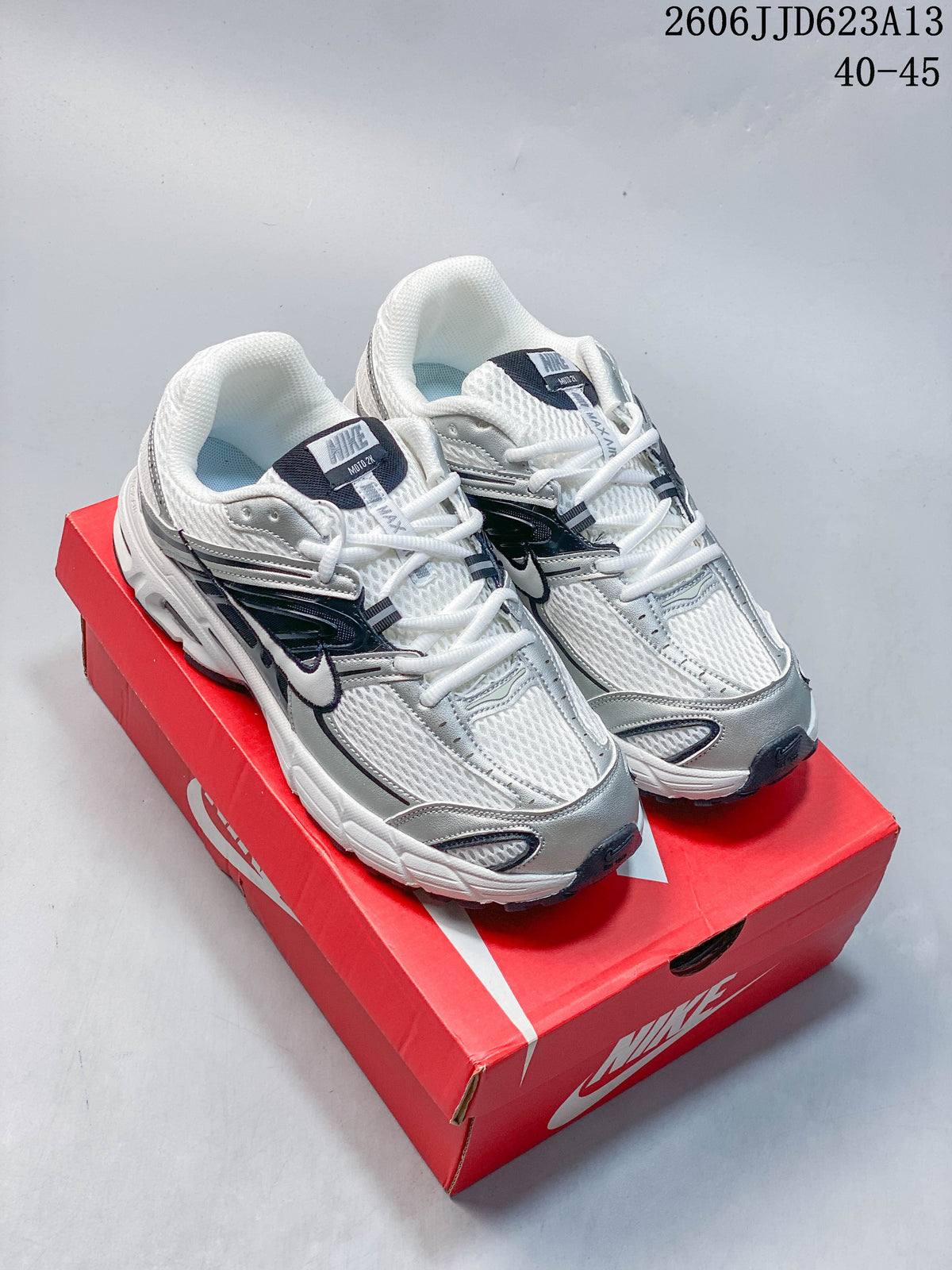 Pair of white, silver, and black Nike Air Max Moto 2K sneakers on a red shoe box
