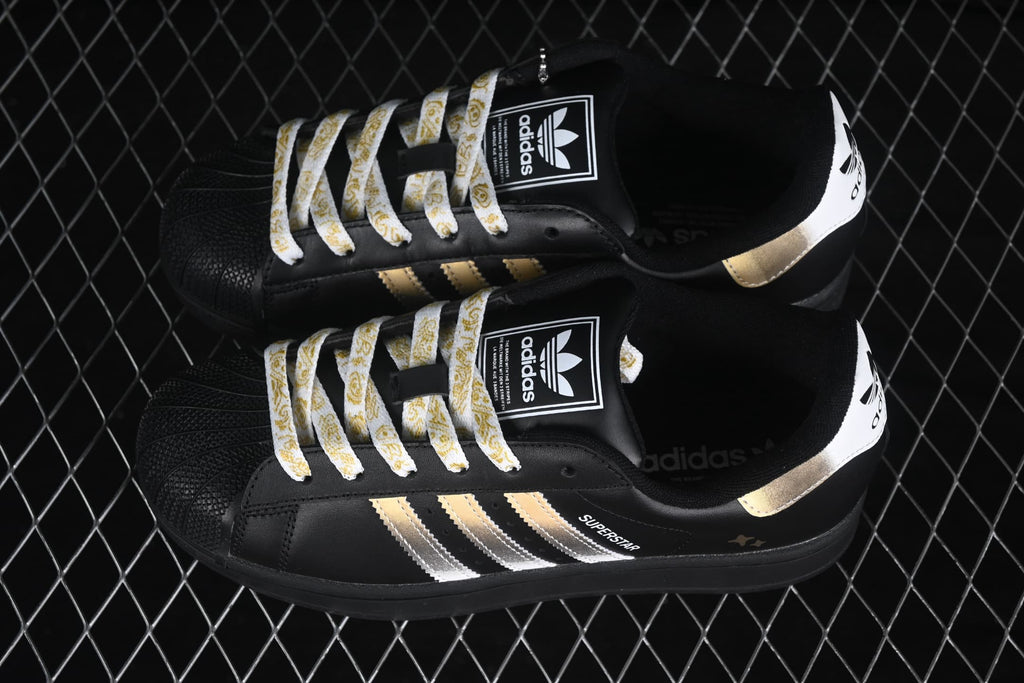 Pair of black adidas Superstar II sneakers with metallic gold and silver stripes and patterned white laces.