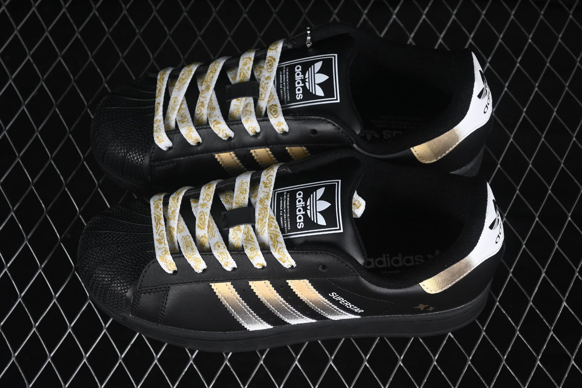 Pair of black adidas Superstar II sneakers with metallic gold and silver stripes and patterned white laces.