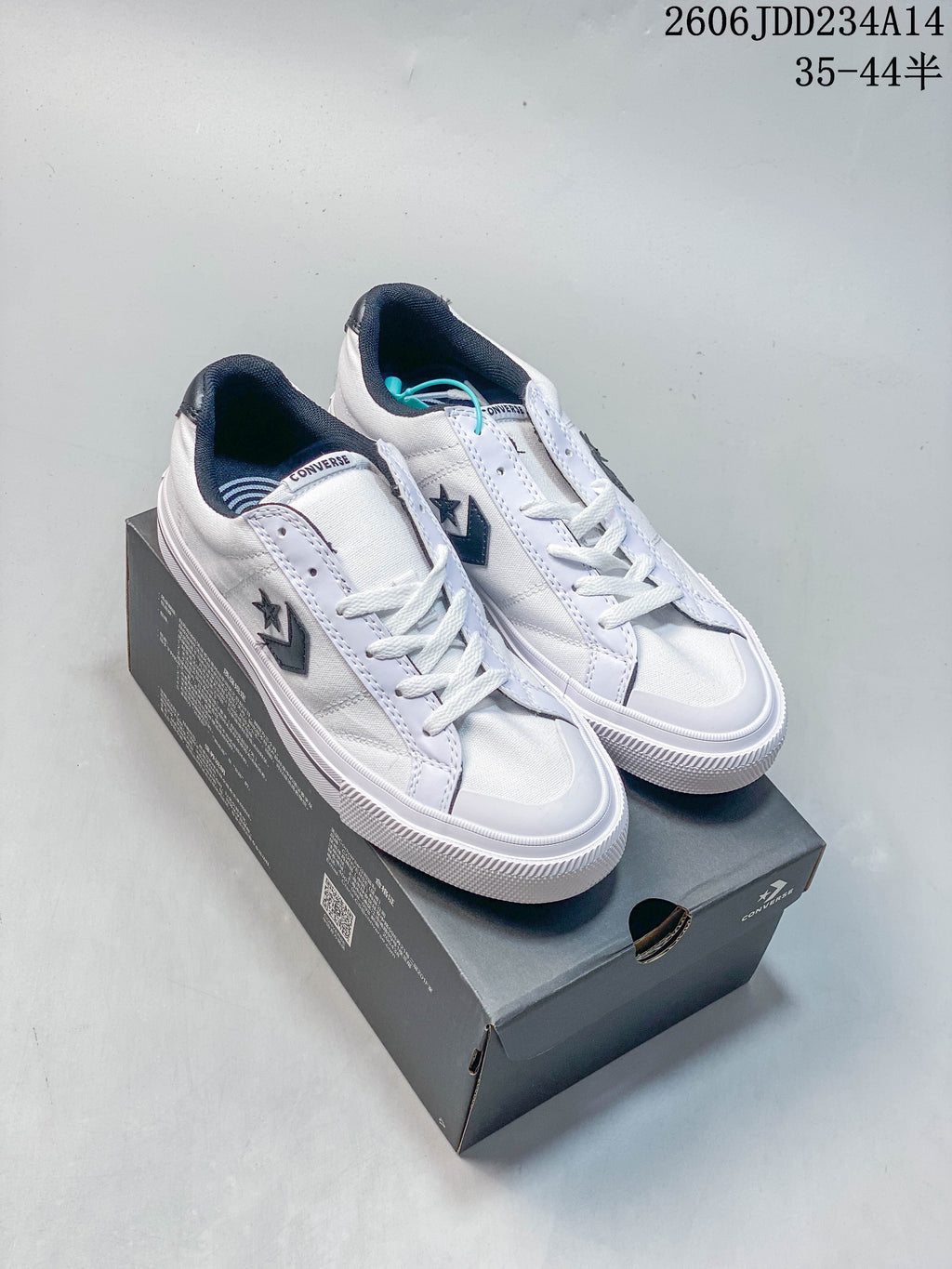 White Converse low-top sneakers with navy accents displayed on a shoebox