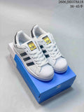 White Adidas Superstar sneakers with black stripes and shell toes, shown on a blue box