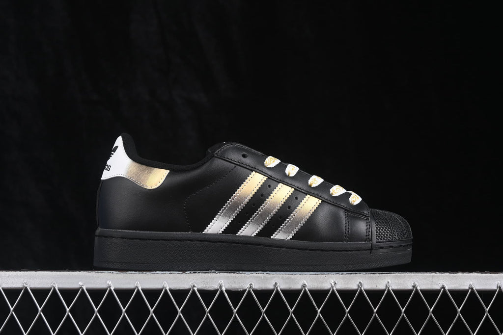 Side profile of a black adidas sneaker showing metallic stripes, a gold heel accent, and a shell toe.