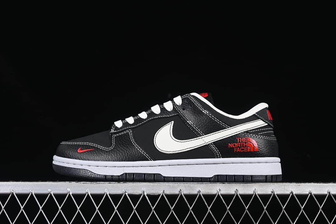 Side view of a black low-top sneaker with white laces, a white Swoosh, red accents, and a white midsole.
