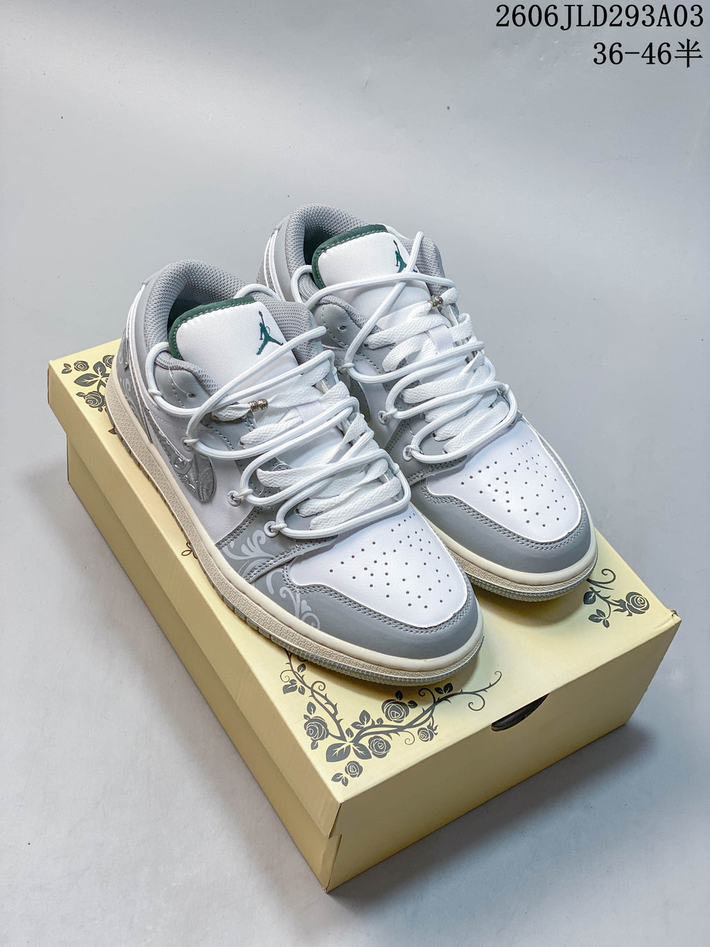 Pair of white and gray Jordan low-top sneakers on a patterned box; overlay shows code 2606JLD293A03 and a size range.