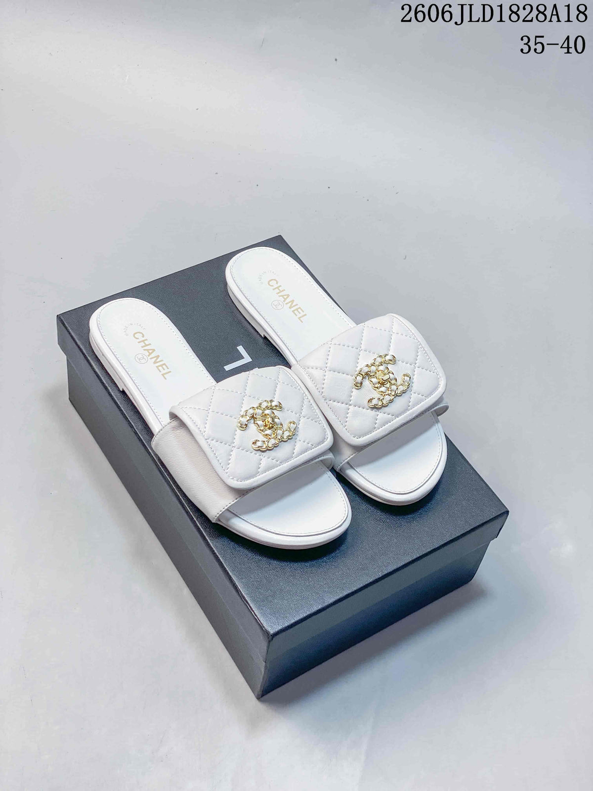 Pair of white quilted slide sandals with gold-tone Double C-style ornaments, displayed on a box.