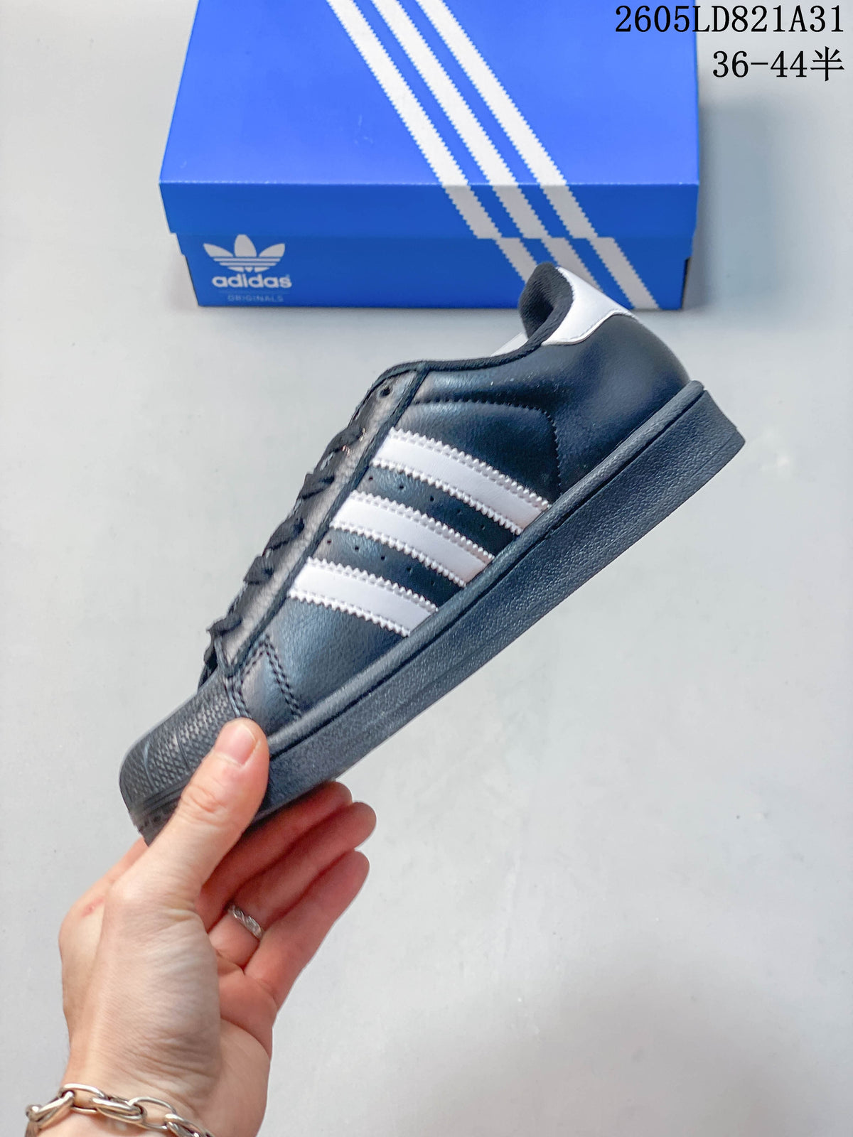 Side view of a dark Adidas Superstar sneaker with white stripes and a textured shell toe.