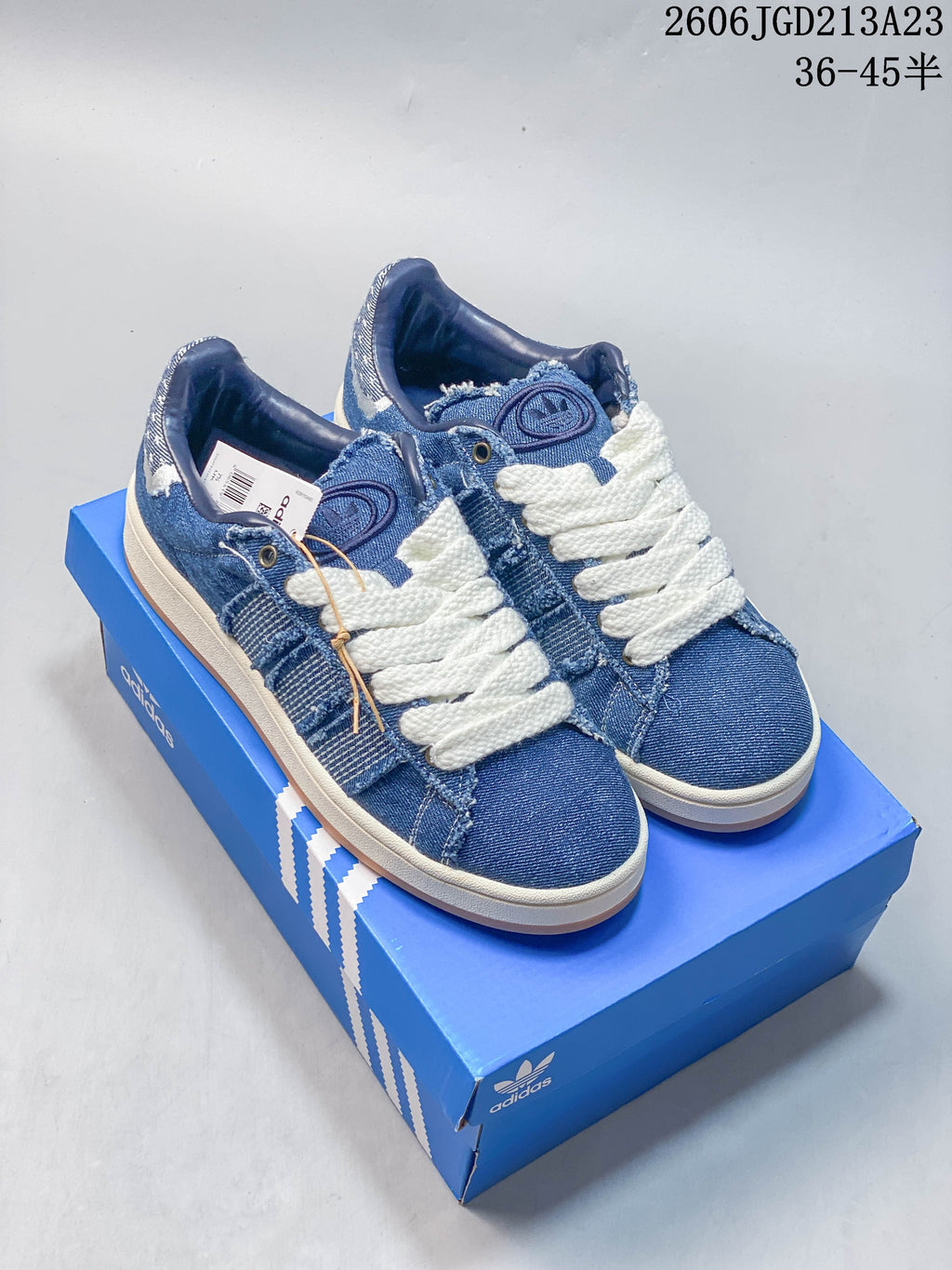 Blue denim-style Adidas Campus 00s sneakers with oversized white laces, shown on a blue shoe box.