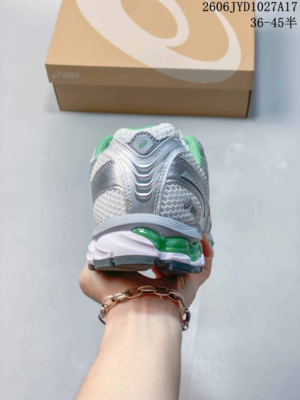 Rear view of a silver-toned sneaker with green heel accents