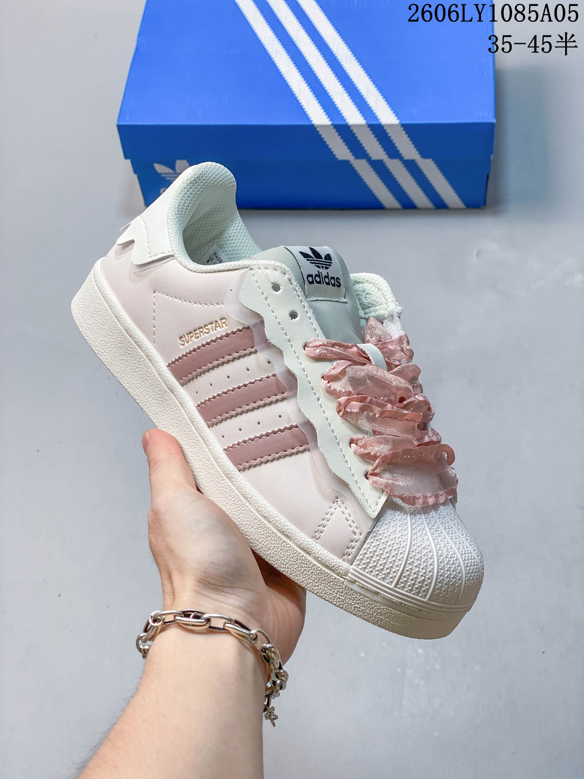 Close-up of a cream Superstar sneaker with pink side stripes and decorative ruffle-style laces