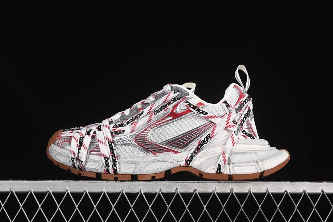 Side view of white Balenciaga 3XL sneakers with red and gray accents, logo-patterned laces, and brown-toned outsoles