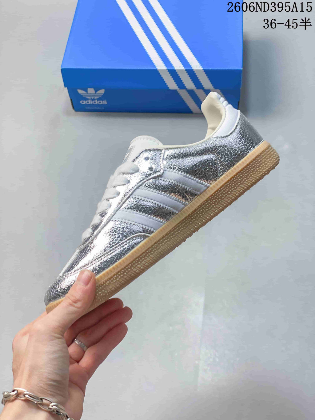 Side view of a silver Adidas Originals low-top sneaker with white stripes and a gum-colored sole