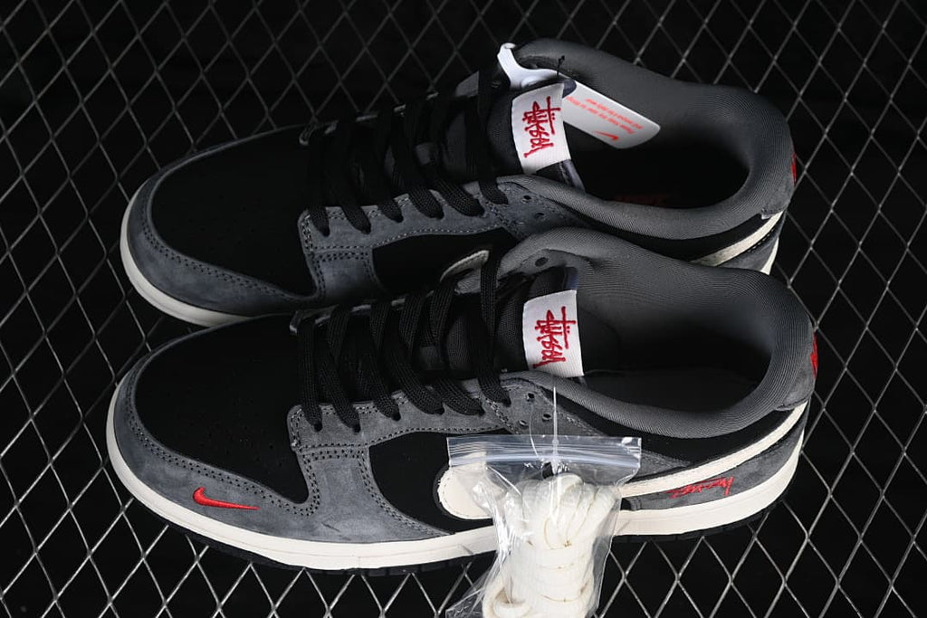 Pair of black and grey low-top sneakers with black laces, red accents and a bag of white laces