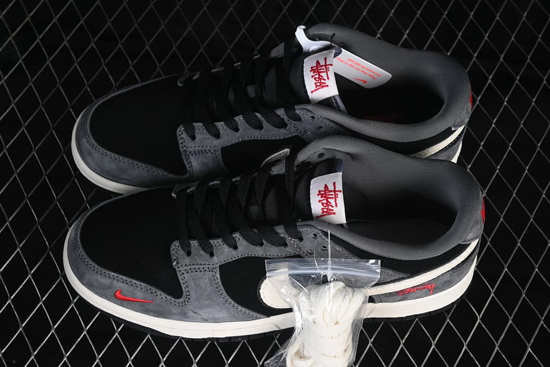 Pair of black and grey low-top sneakers with black laces, red accents and a bag of white laces