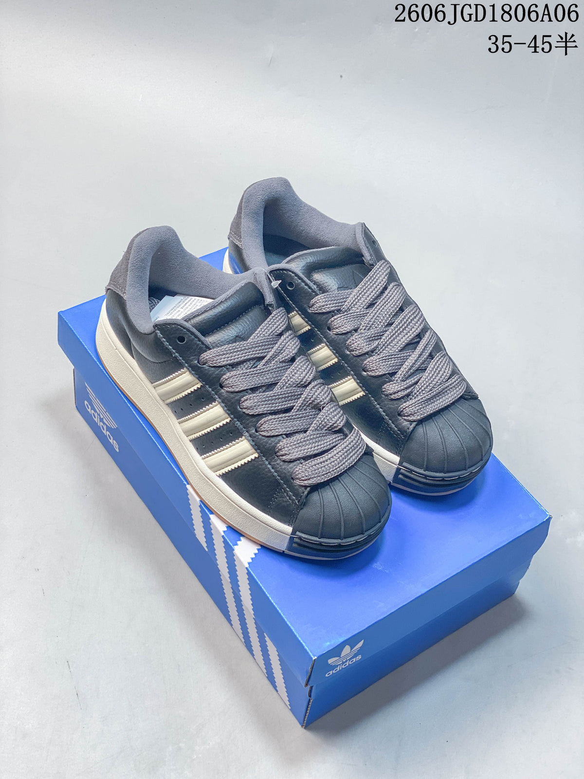 Pair of dark grey Adidas Superstar low-top sneakers with off-white stripes, grey laces, shell toes, and gum outsoles, shown on a blue shoe box.