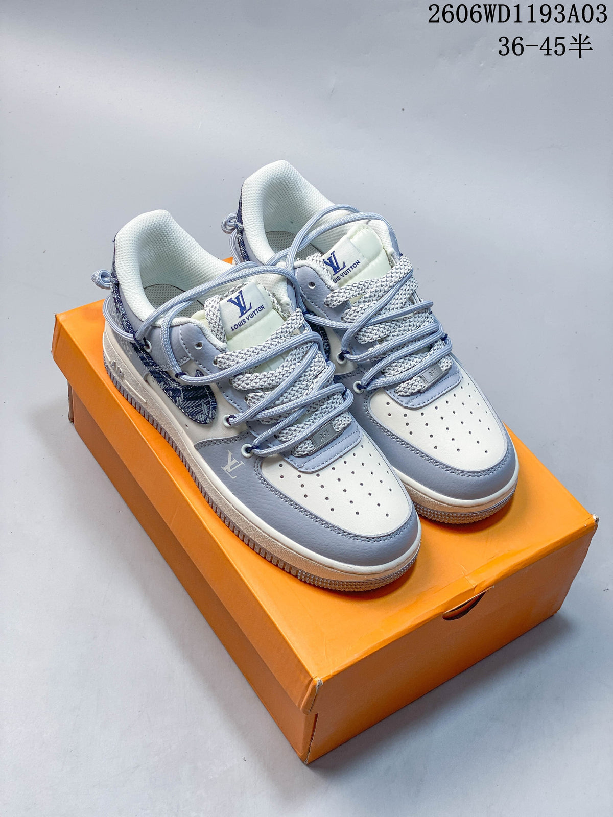 Pair of white and pale gray low-top sneakers with blue patterned panels and layered laces, shown on an orange box.