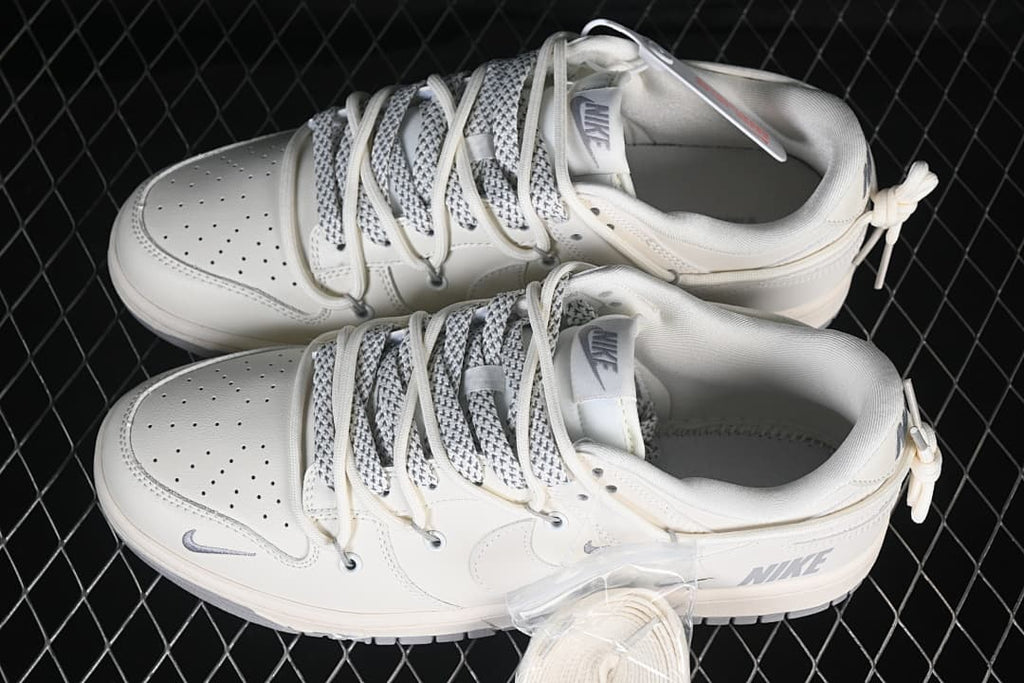 Pair of cream and gray Nike SB Dunk Low sneakers with patterned laces and heel cords