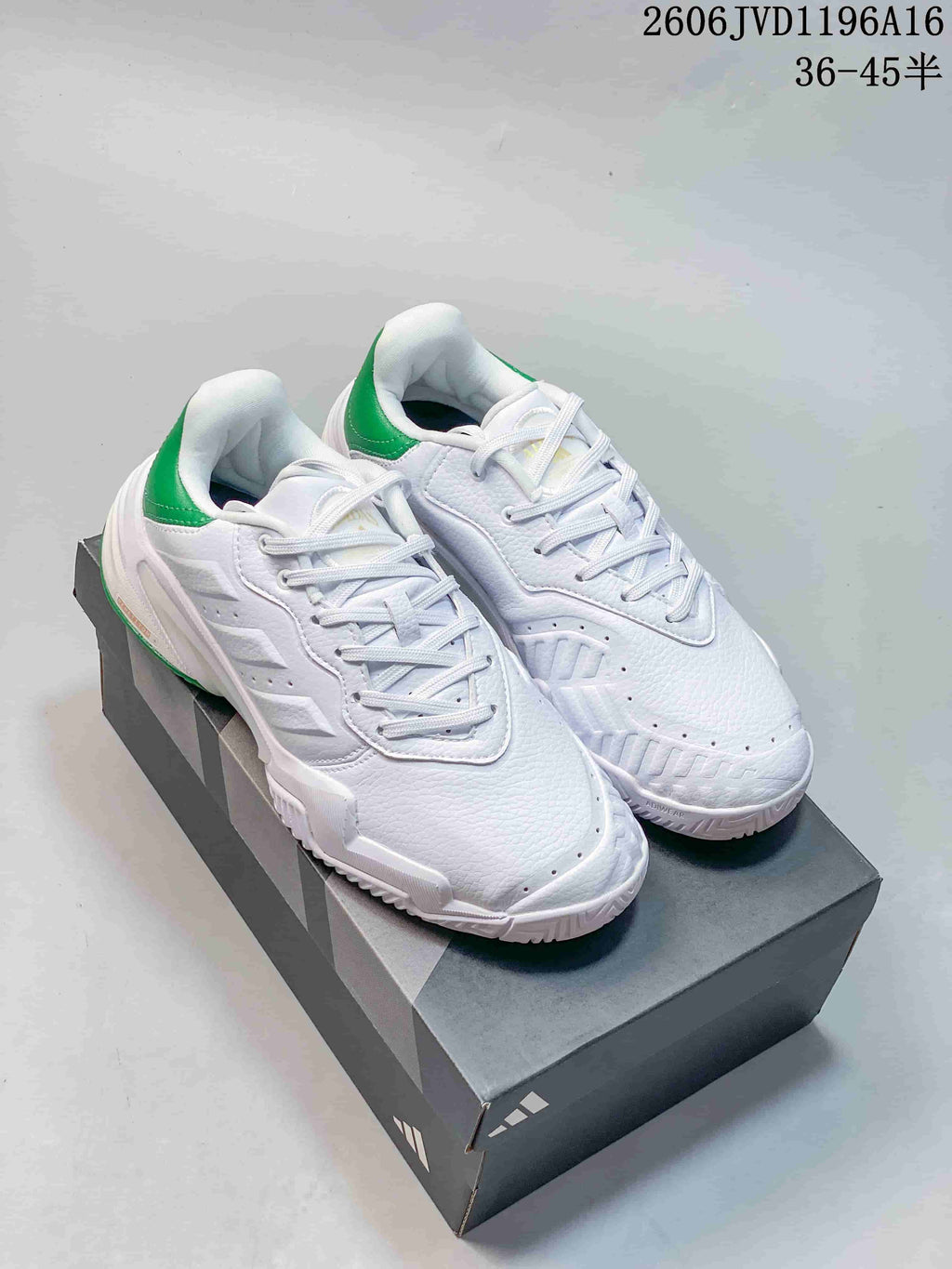 Pair of white Adidas Barricade tennis shoes with green heel accents on a shoebox.