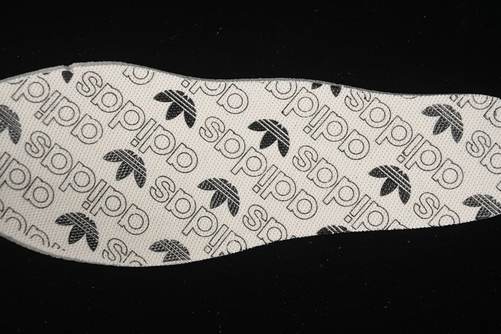Close view of an insole printed with adidas Trefoil and wordmark patterns.