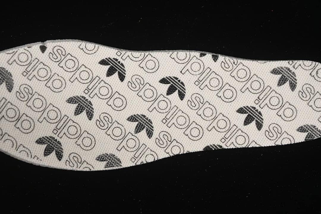 Close view of an insole printed with adidas Trefoil and wordmark patterns.