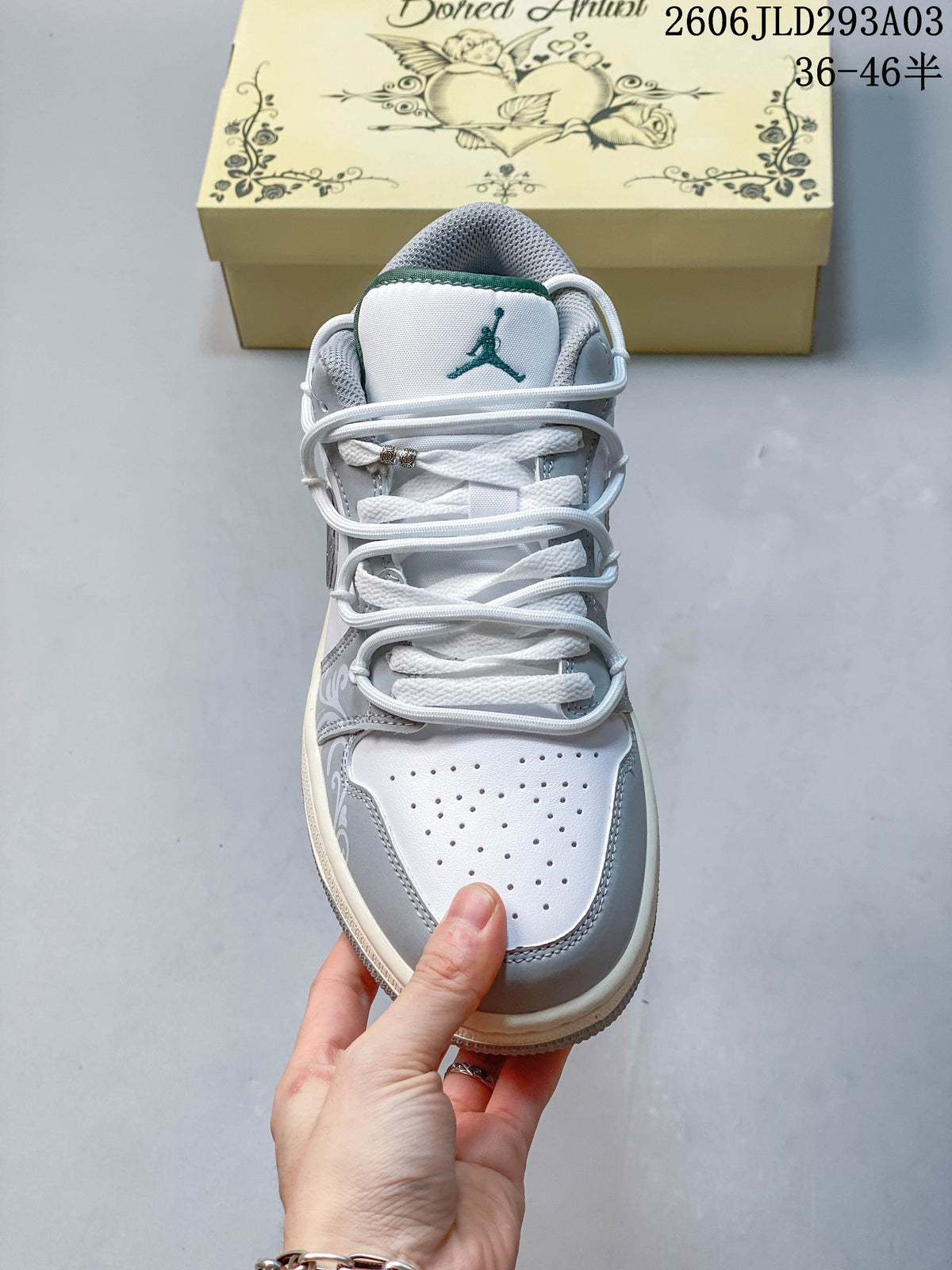 Front view of a white and gray sneaker with perforations, white laces, and a green tongue accent; overlay shows a size range.