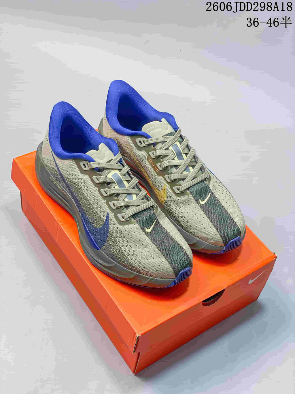 Pair of gray-green Nike ReactX Pegasus Plus Next Nature running shoes with blue accents, displayed on an orange shoebox