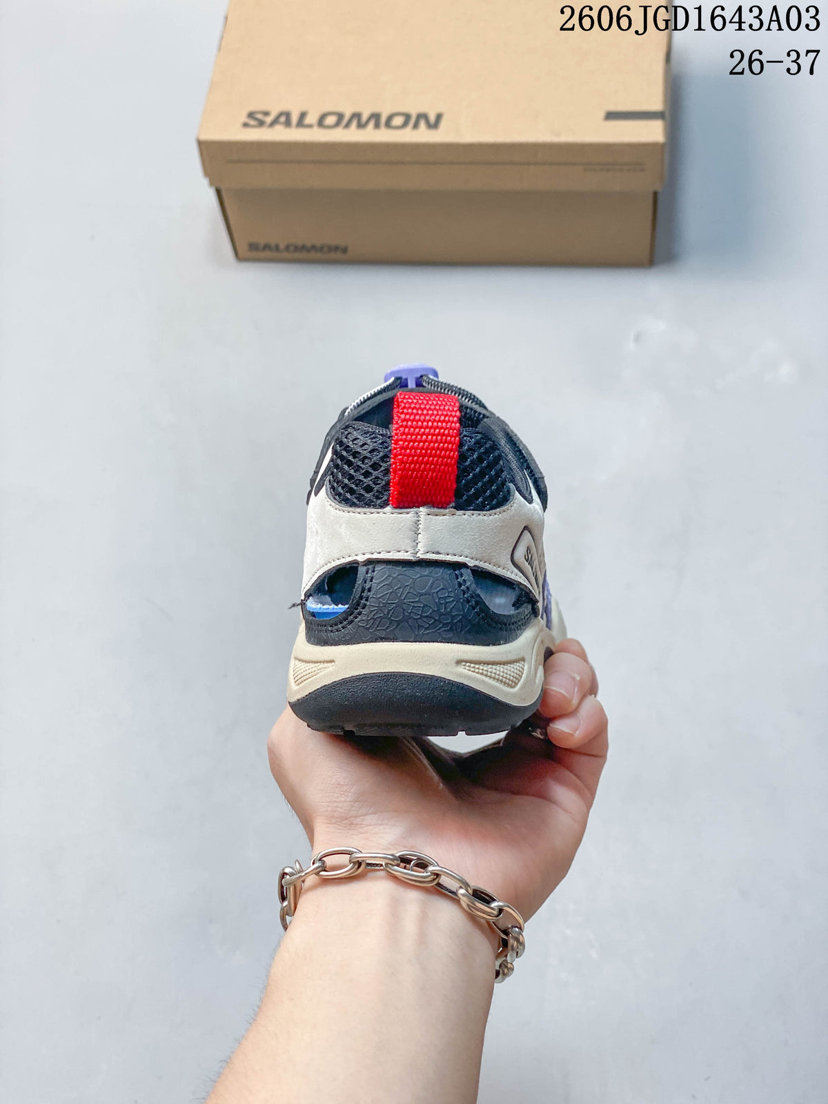 Rear view of a cream and navy Salomon kids' sneaker with a red pull tab