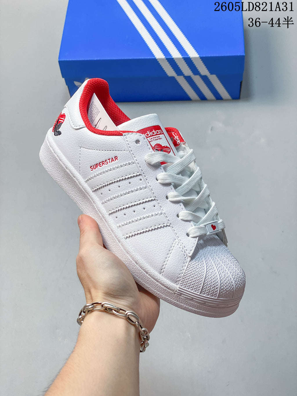 White adidas Superstar sneaker with red accents and a textured shell toe.