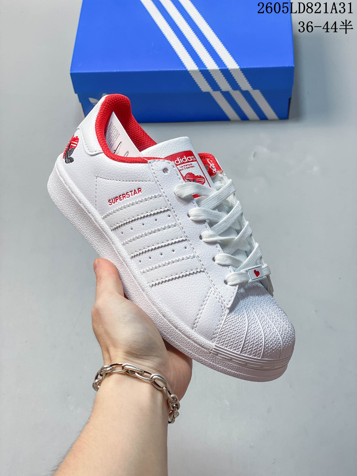 White adidas Superstar sneaker with red accents and a textured shell toe.