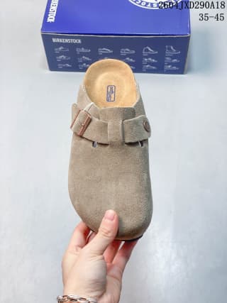 Top view of a beige suede closed-toe clog with a metal buckle, shown in front of its blue shoe box.
