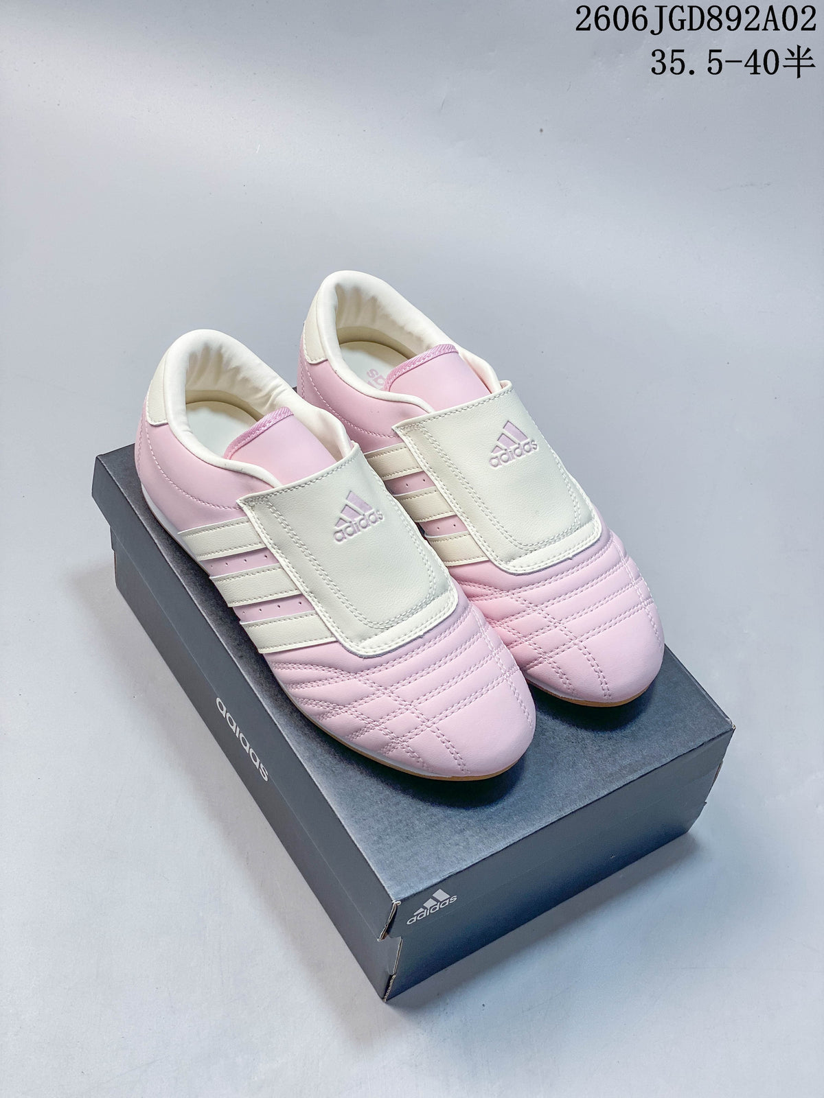 Pink and off-white Adidas Taekwondo shoes shown from the front on a shoebox
