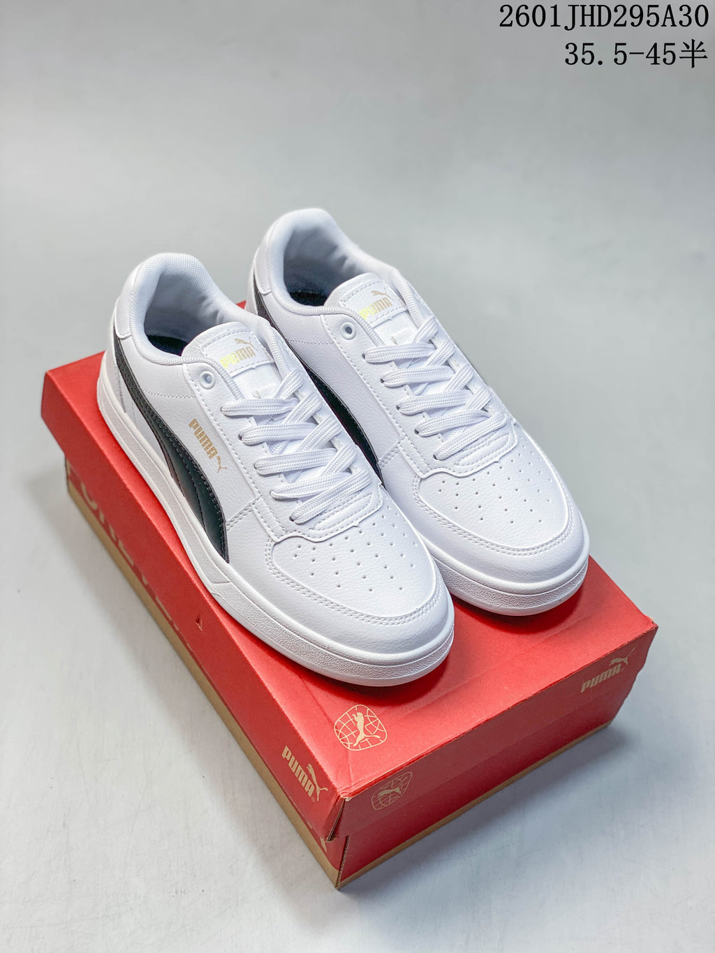 Pair of white Puma Caven 2.0 low-top sneakers with dark side stripes on a red shoe box