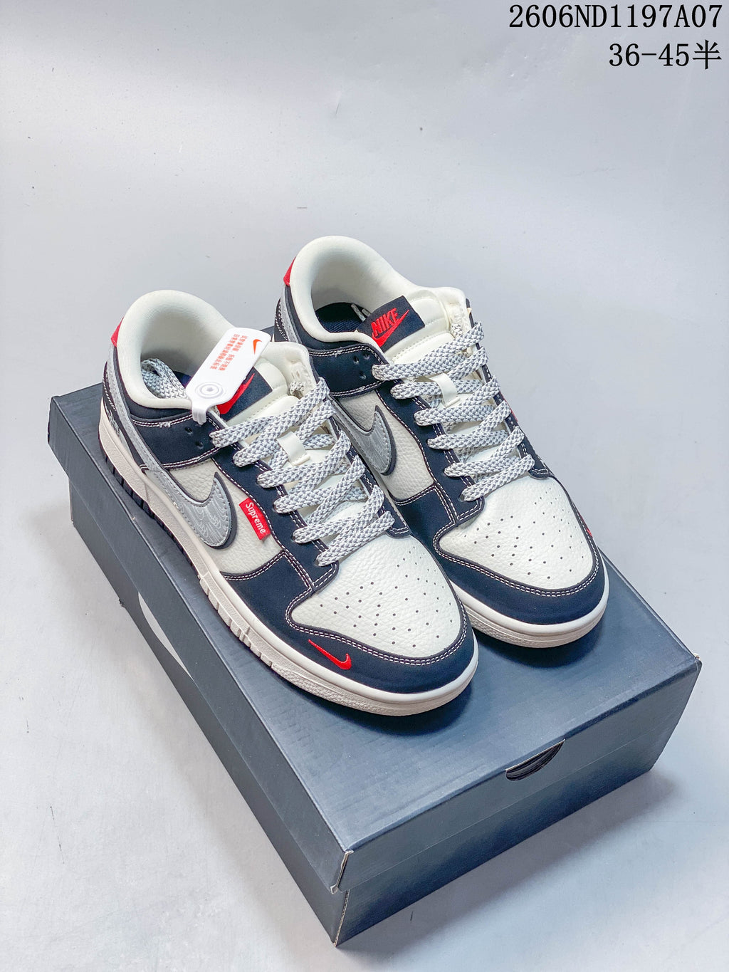 Pair of white, navy, and gray Nike SB Dunk Low sneakers with red accents on a shoe box