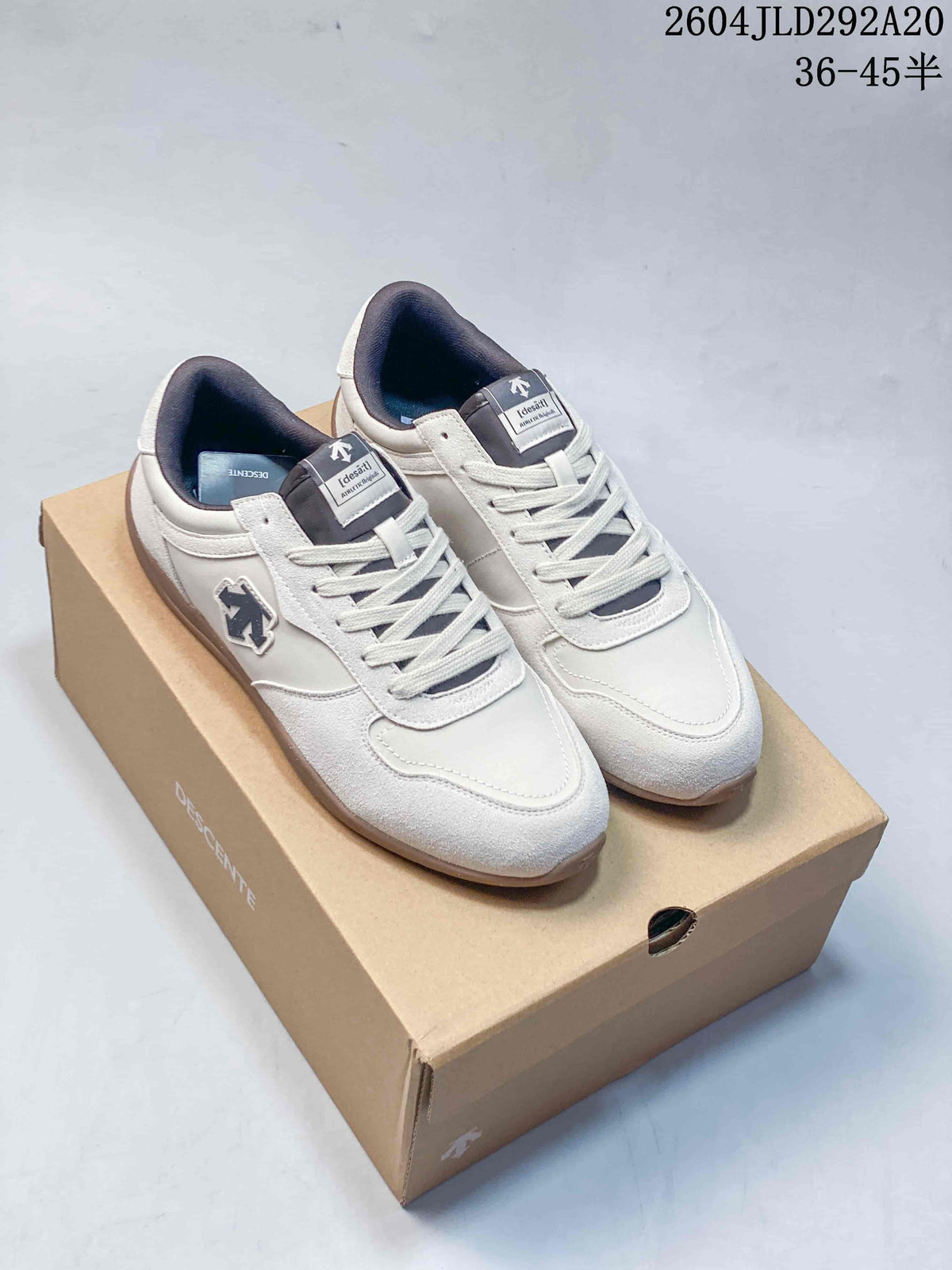 Pair of white Descente low-profile sneakers with dark tongue and collar accents.
