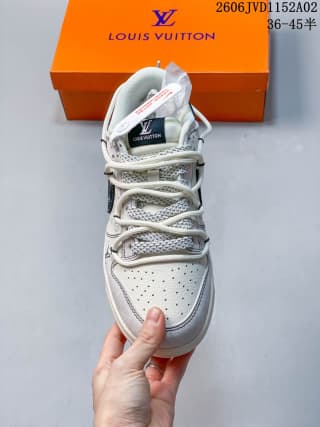 Front view of white and gray low-top sneakers with dark blue accents, perforated toe box, rope-style laces, and an orange shoe box behind them.