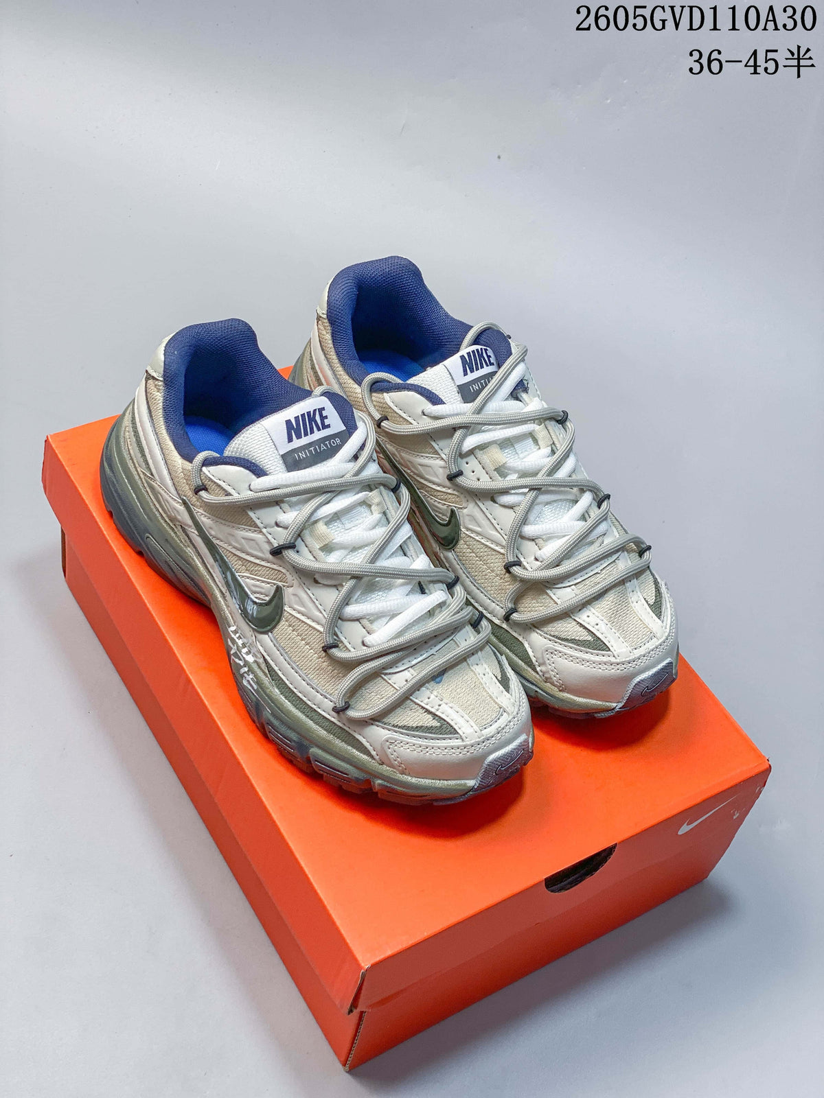 Pair of cream, silver-toned and blue Nike Initiator sneakers on an orange shoebox