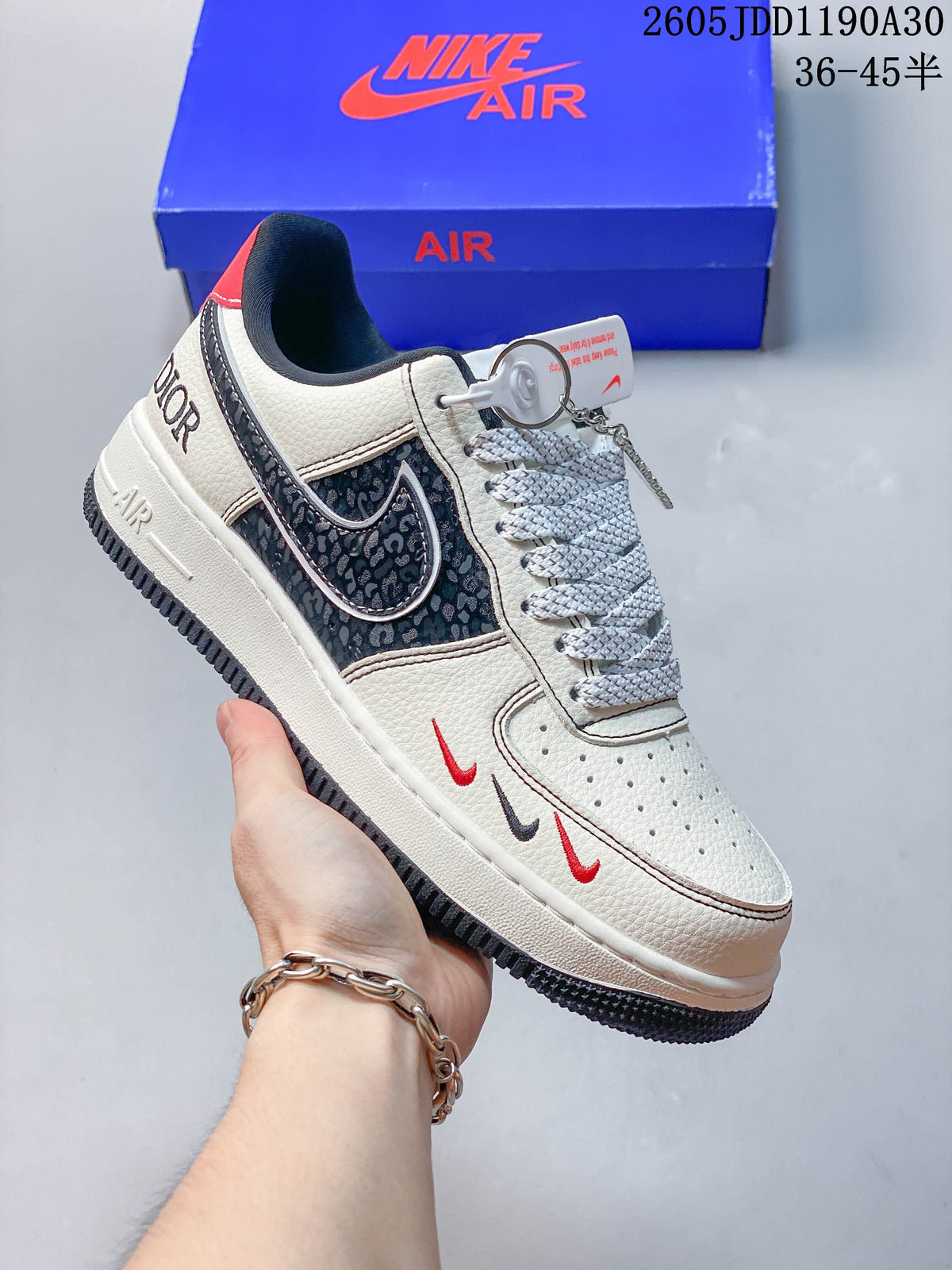 Side view of a white low-top sneaker with dark patterned panels, red details, and a blue box
