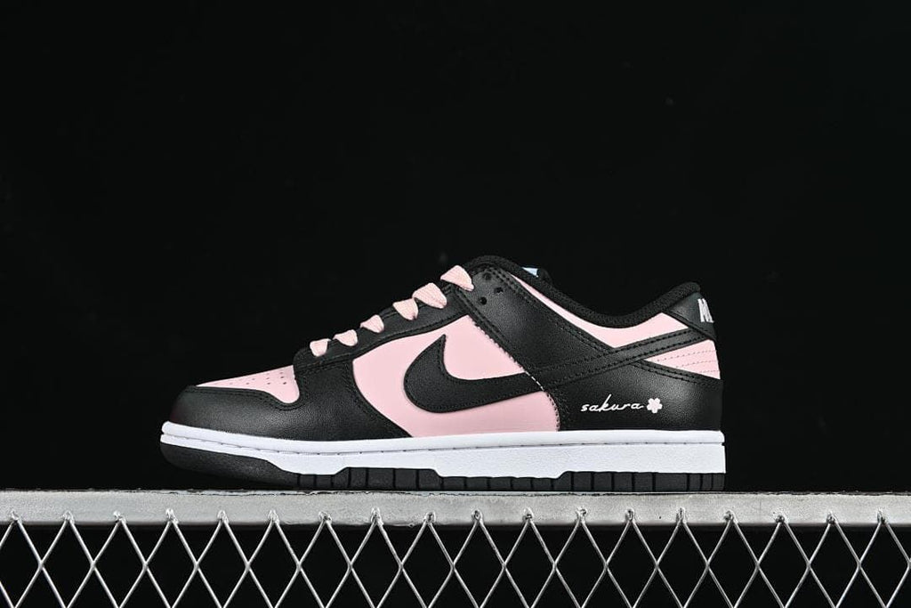 Side view of a black and pale pink low-top Dunk sneaker with white midsole and sakura-style heel embroidery