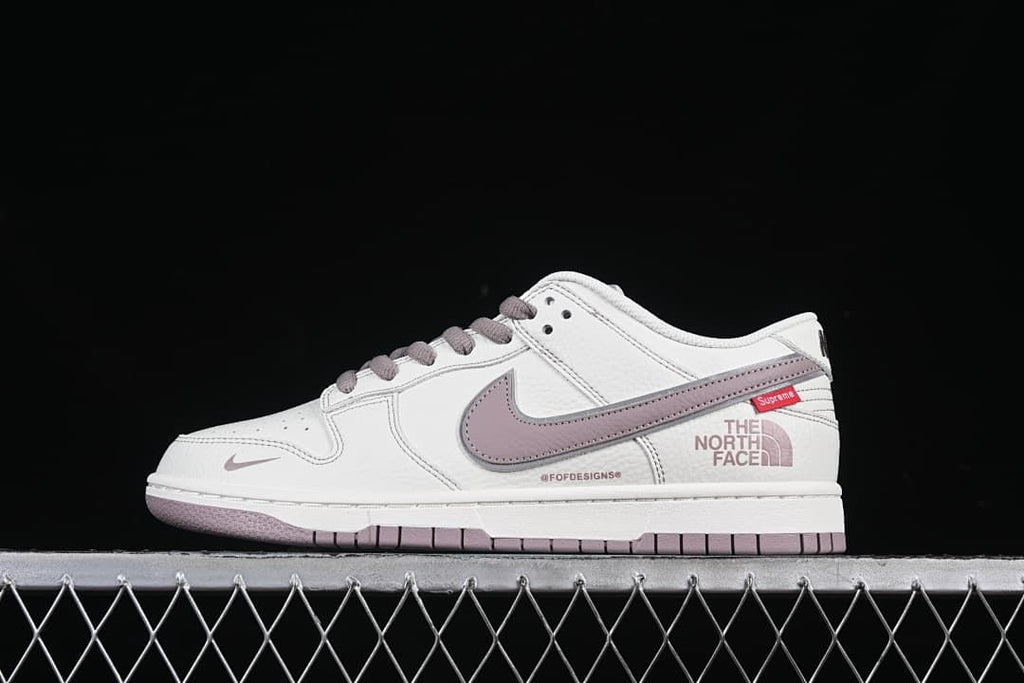Side view of white Nike SB Dunk Low sneakers with mauve accents and Supreme and The North Face graphics