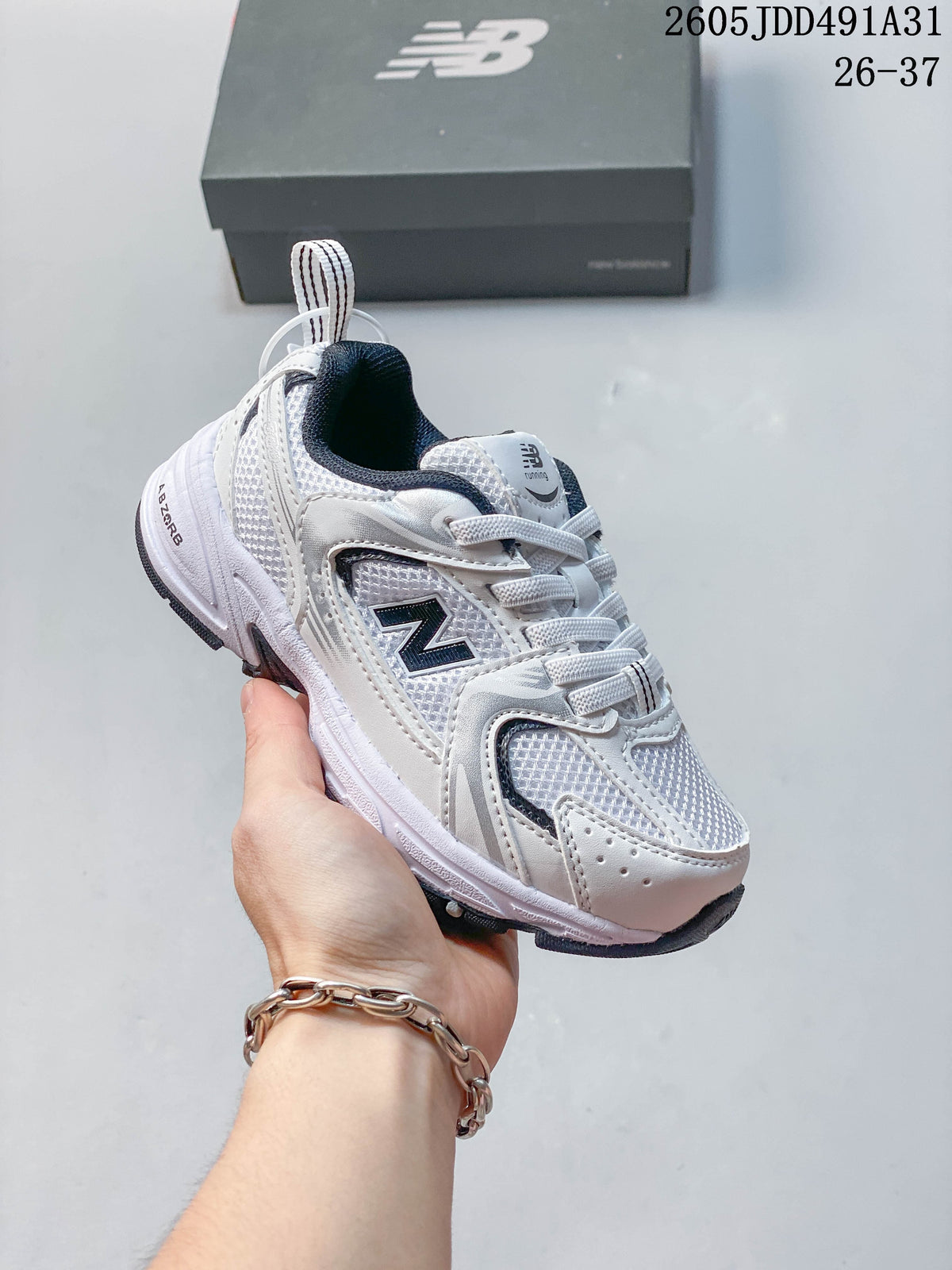 Light-colored kids' New Balance 530 lace-up sneaker shown in hand, with a shoebox behind it.