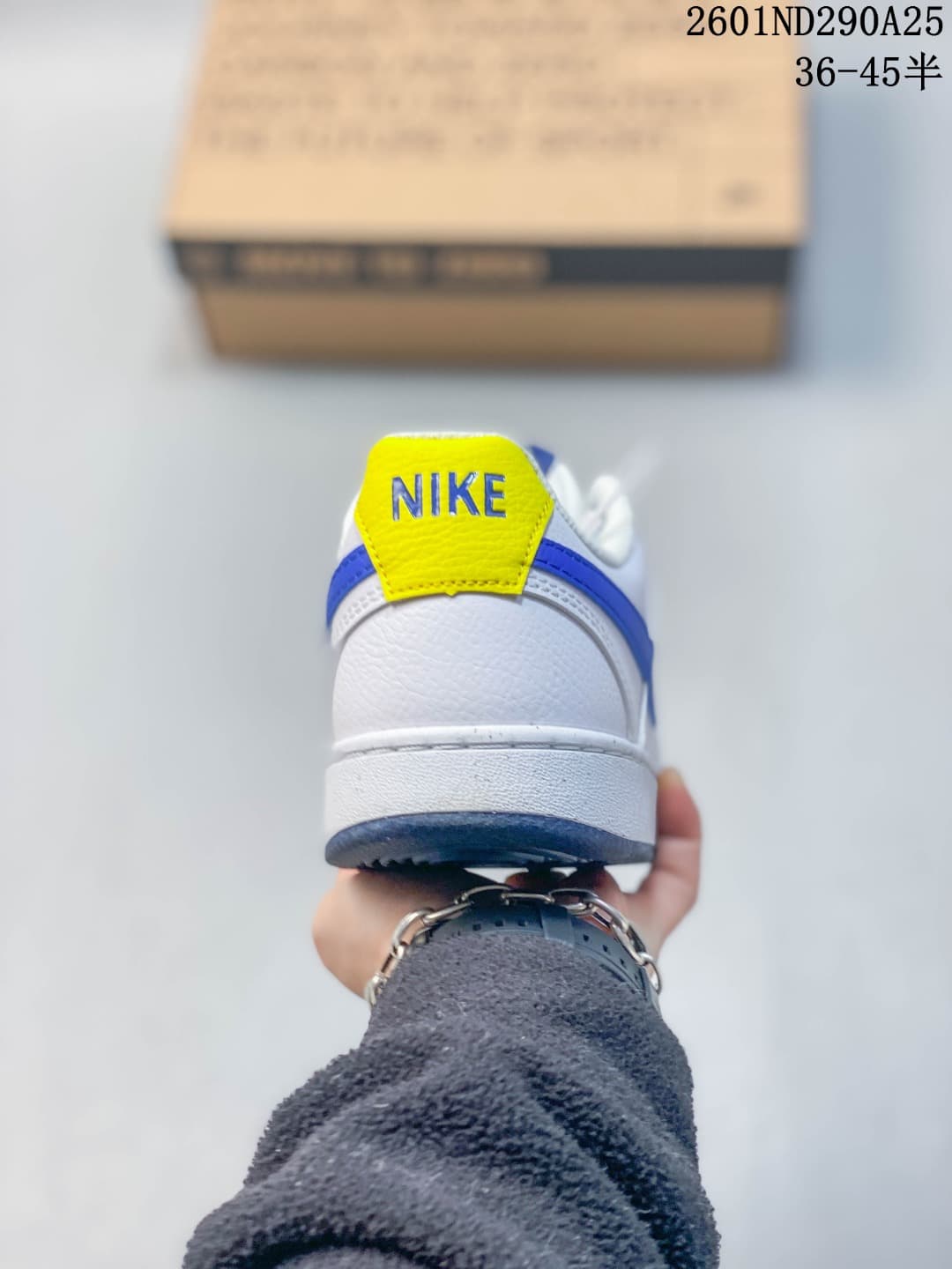 Rear view of the white sneaker with a yellow heel tab and blue trim.