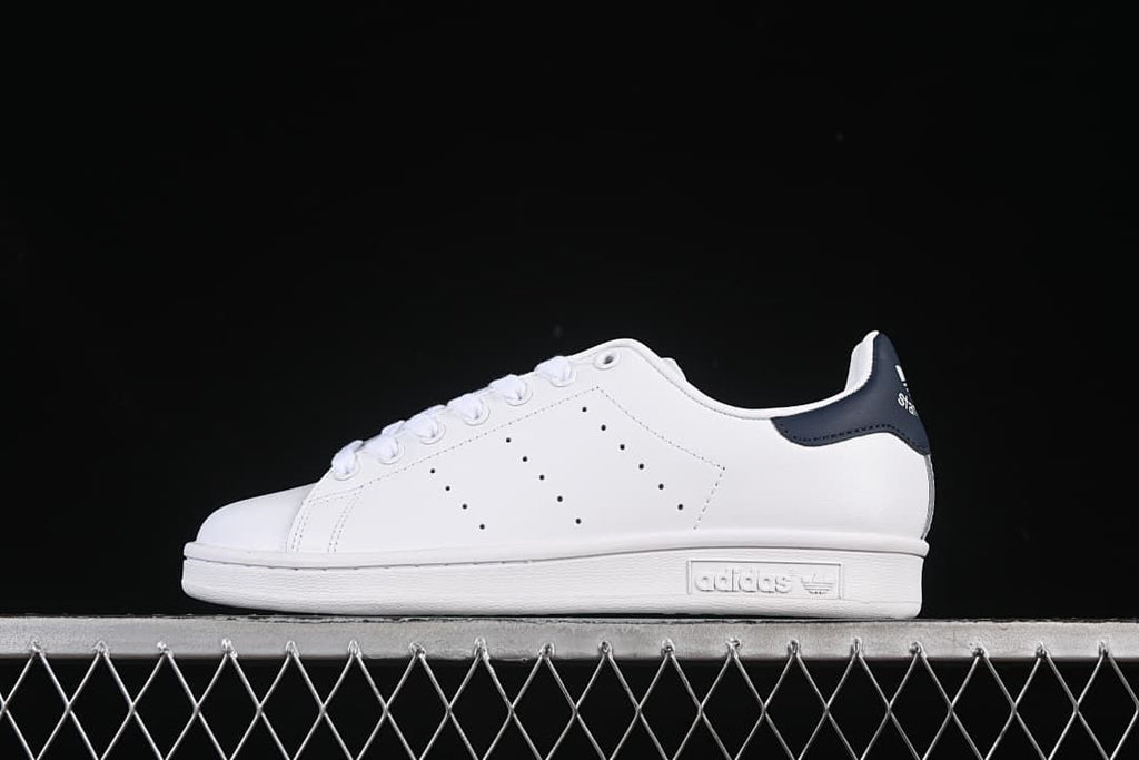 Side view of a white adidas Stan Smith sneaker with a navy heel tab.
