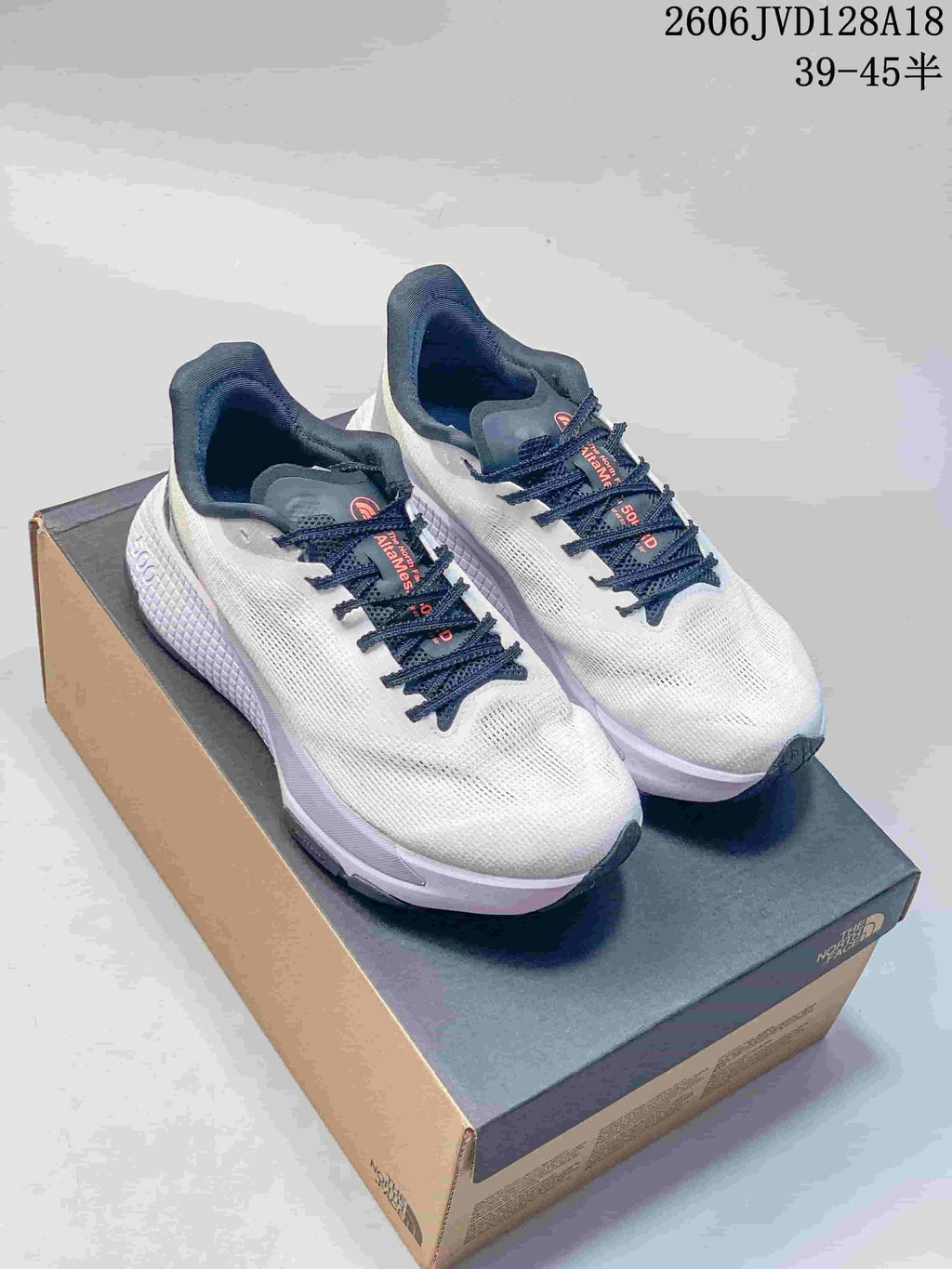 Pair of white The North Face Alta Mesa 500 running shoes with navy laces and pale lavender accents on a shoe box.